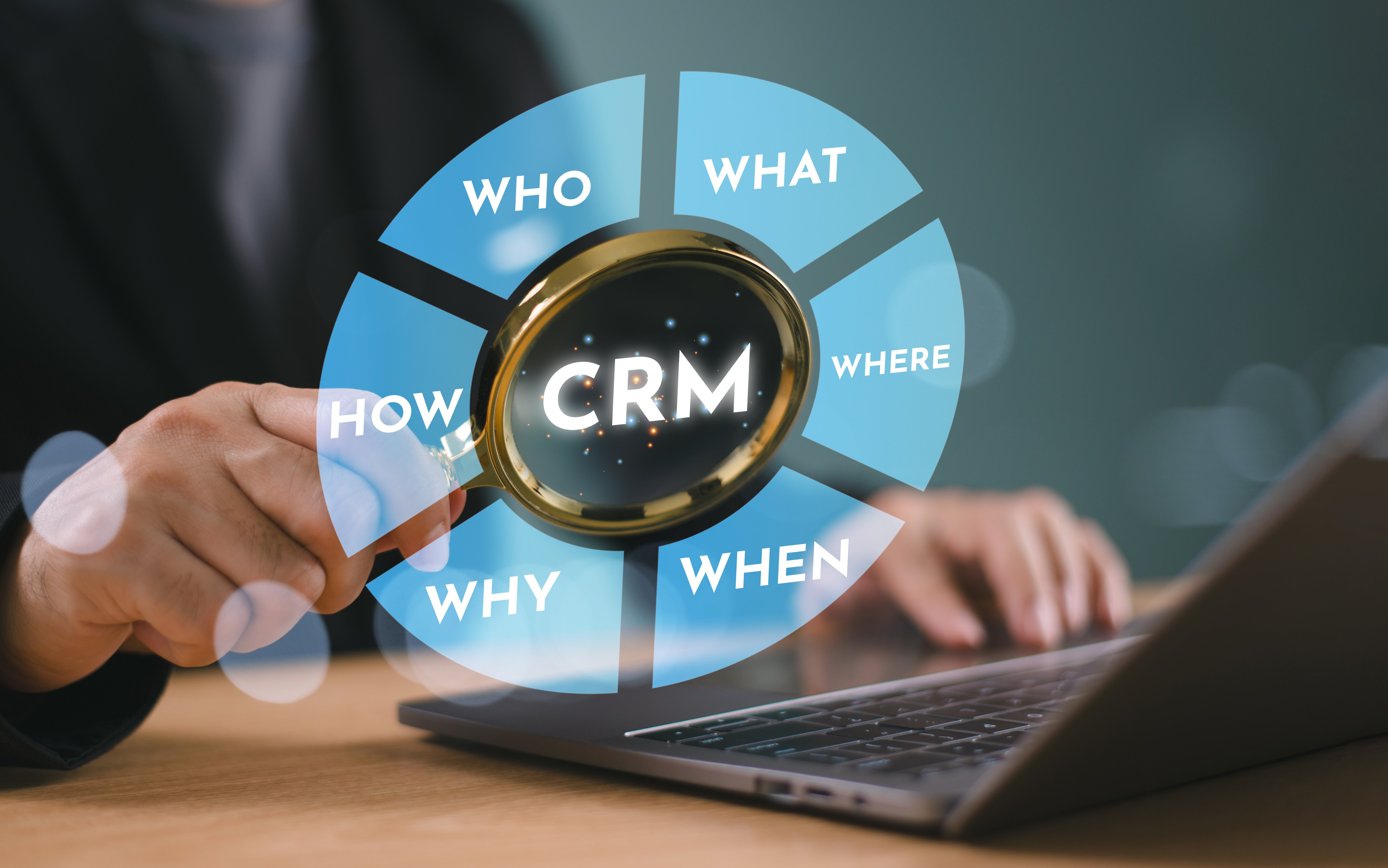 CRM concept with a magnifying glass highlighting Customer Relationship Management, surrounded by key questions: Who, What, Where, When, Why, and How. A business professional working on a laptop in the background, symbolizing data-driven decision-making and CRM strategy.